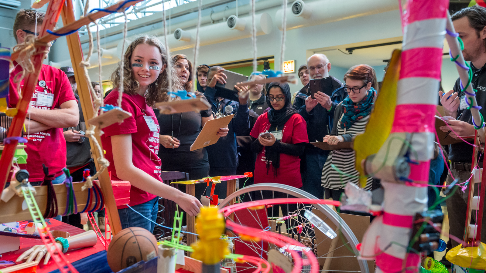 A student from Glenbard South High School provides a narrative of the ball’s journey through the machine as onlookers and judges watch at the Rube Goldberg Machine Contest.