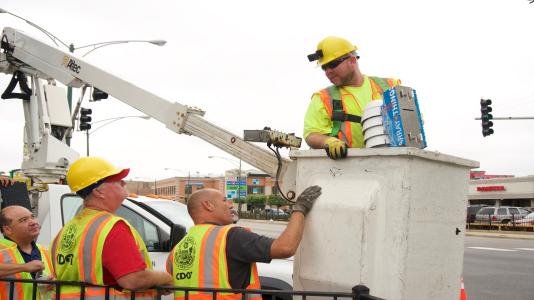Workers from the Chicago Department of Transportation install a node for the Array of Things, a distributed sensing network for urban environments, at Damen and Archer avenues in downtown Chicago. (Image by Rob Mitchum/University of Chicago.)