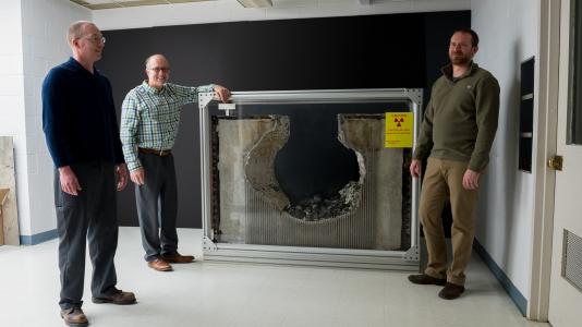 Nathan Bremer, Mitch Farmer (center) and Jeremy Licht (right) highlight a piece of concrete eroded in tests by corium — the lava-like material formed when uranium fuel rods in the reactor core melt, along with their protective metal cladding. The team’s tests helped nuclear plant operators avoid $1 billion in expenses. Not shown: Stephen Lomperski and Dennis Kilsdonk. (Image by Argonne National Laboratory.)