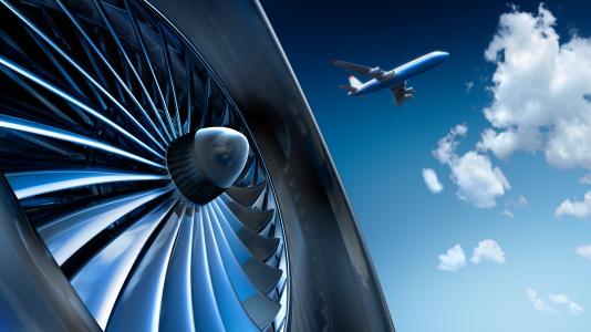 Airplane engine closeup photo with ascending airplane in background against blue sky and white clouds. (Image by Shutterstock/peterschreiber.media.)  
